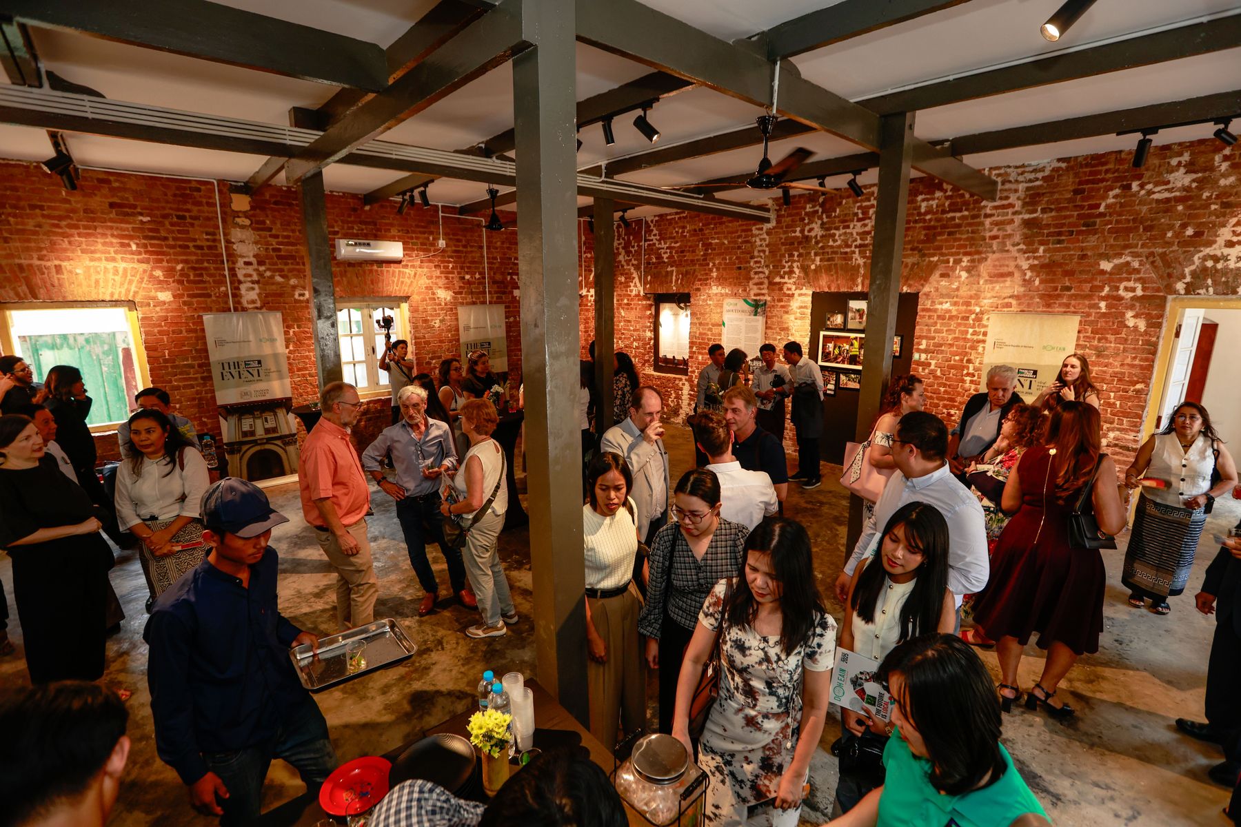 Guests fill the restored hall of the Thanlyin HERitage Centre at its launch, beneath timber roof beams and exposed brick walls hung with exhibition panels